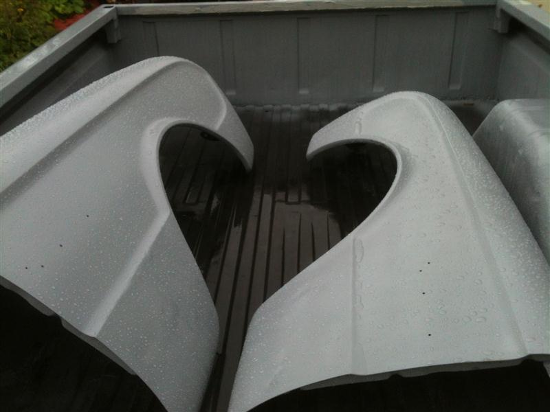 Two white car fenders with cutouts for wheels, sitting in the bed of a pickup truck