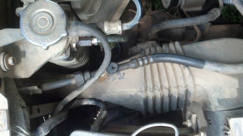 1996 Ford Bronco - Close-up view of a vehicle's power steering rack and pinion assembly, showing hoses and a warning cap.