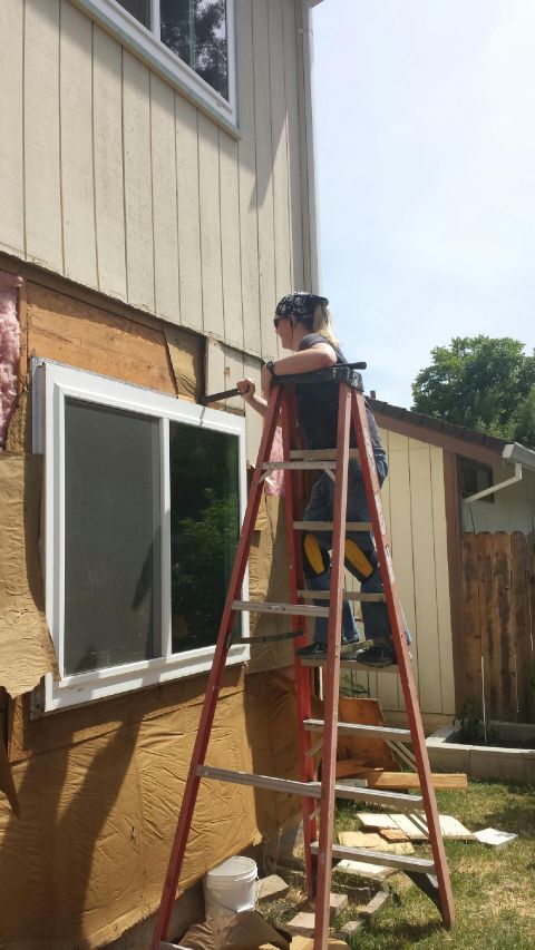 1989 Ford Bronco - A person on a ladder works on the exterior of a house, removing siding near a window.