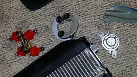 2007 Subaru Impreza - A collection of assorted vehicle parts, including a red fuel rail assembly and a silver vacuum actuator, are displayed on a carpeted surfac…