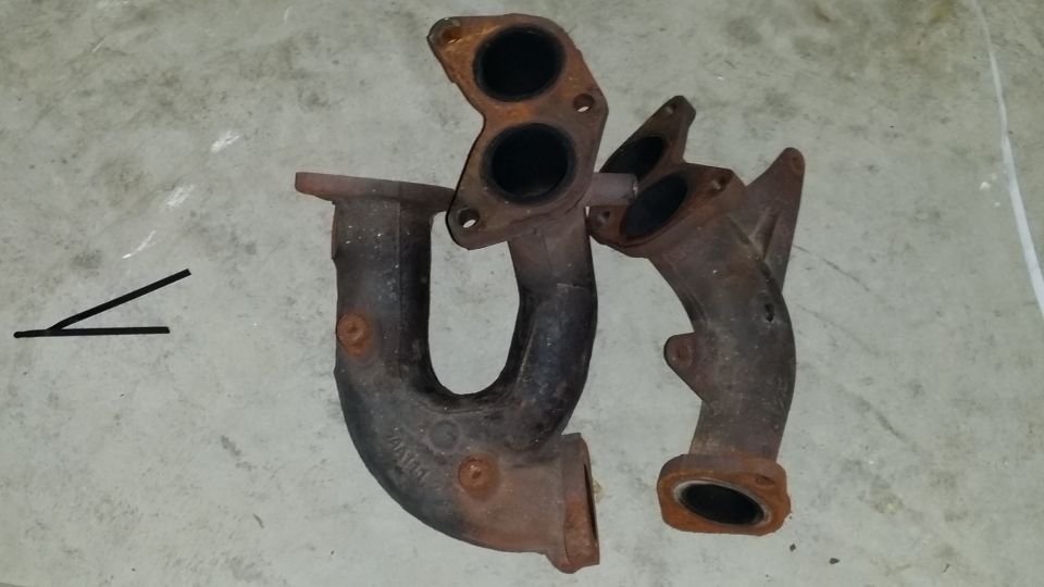Two rusty exhaust manifold sections on a concrete floor
