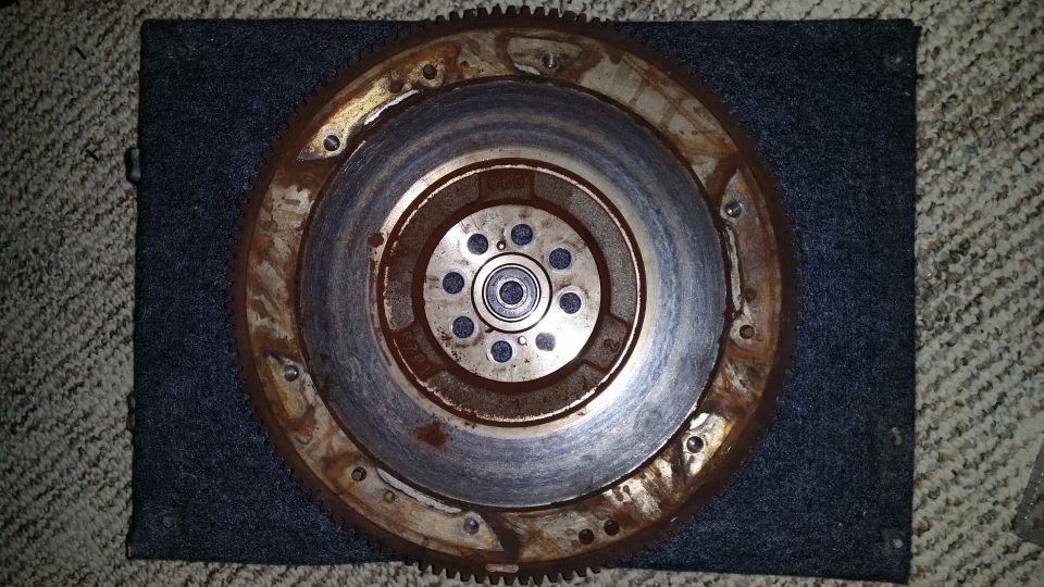 Rusty flywheel with a bearing in the center, resting on a dark mat