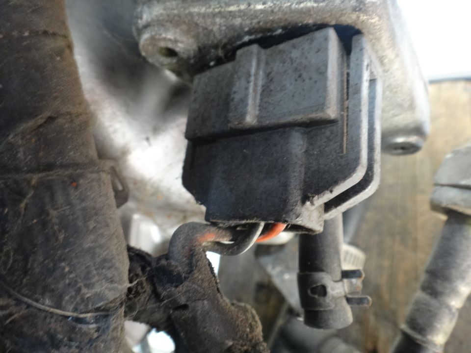 Close-up of a gray electrical connector with orange and black wires attached to a black harness