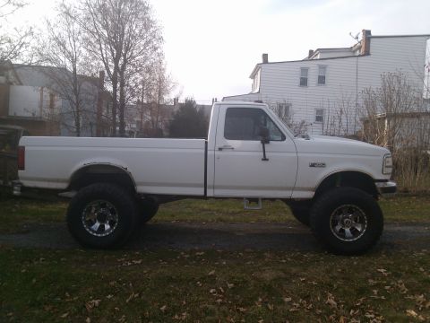 1995 Ford F-350 - This lifted pickup truck is shown from the side, parked outdoors on a grassy area with houses in the background.