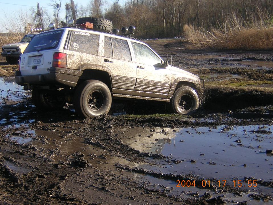 Muddy 1996 Jeep Grand Cherokee stuck in a mud pit, with another truck visible in the background