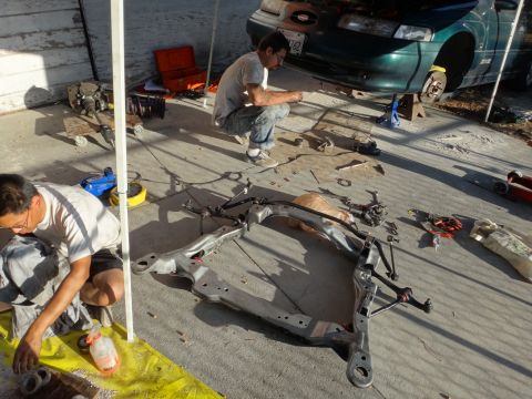 1993 Ford Taurus - Mechanics work on the front suspension of a green 1993 Ford Taurus, with parts laid out on the ground.