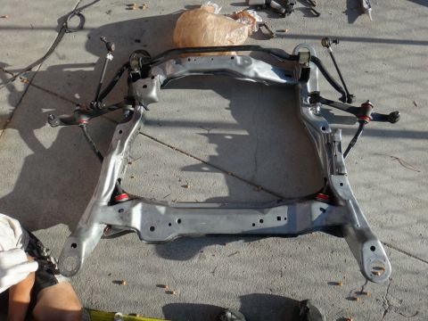 1993 Ford Taurus - A front subframe assembly, likely from a car, is laid out on a concrete surface.