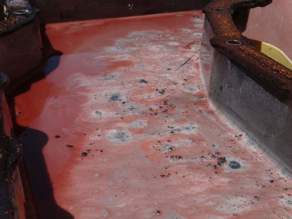 Red liquid with debris in a rusty metal container