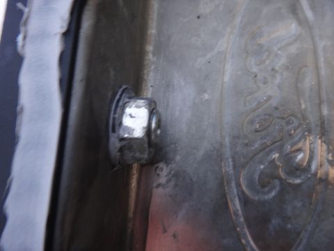 1993 Ford Taurus - A close-up shot shows a bolt securing a metal panel with a Ford emblem embossed on it.
