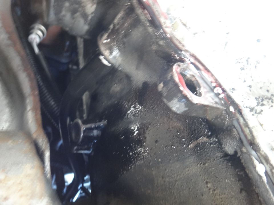 Close-up of greasy, dark metal engine or transmission component with a bolt hole
