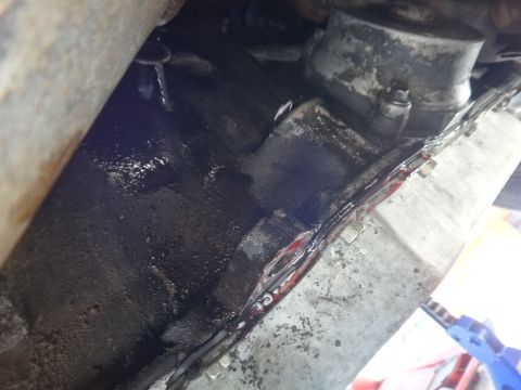 1993 Ford Taurus - Close-up view of a leaking transmission pan gasket with visible red fluid and bolts.