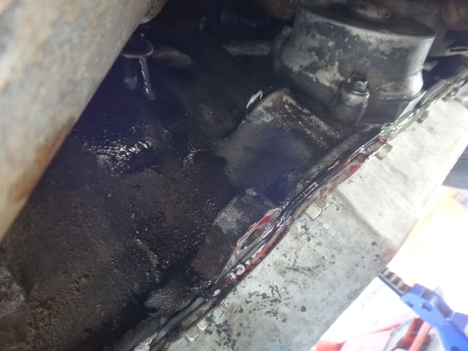 Transmission pan gasket leaking red fluid, showing bolts and metal casing