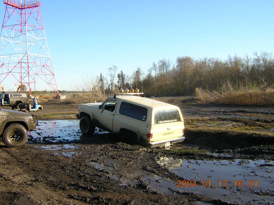tan SUV stuck in mud, another SUV and a golf cart nearby, tall tower in background
