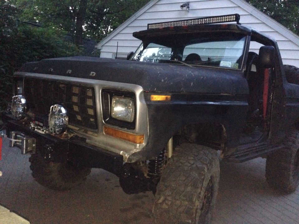 Front end of a black Ford Bronco with a custom grille and light bar. It has aftermarket lights and large tires