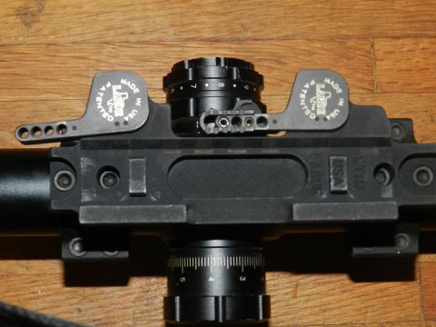 1996 Ford Bronco - A close-up view of a black gun scope mount with adjustable turrets and levers.