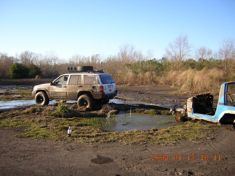 Muddy lifted white Jeep Grand Cherokee winching a stripped blue Jeep out of a mud pit