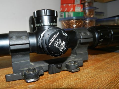 1996 Ford Bronco - A close-up view of a rifle scope, showing its adjustment turrets and a distinctive logo on the side.