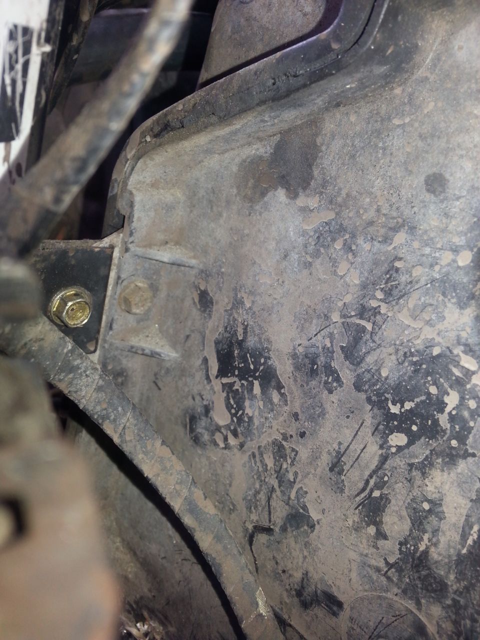 Close-up of a dirty metal bracket with a bolt and nut, part of a vehicle's evaporator box