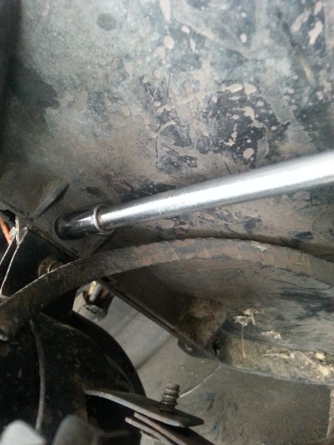 1992 Ford Bronco - A screwdriver is used to access a component on the dirty underside of a vehicle.