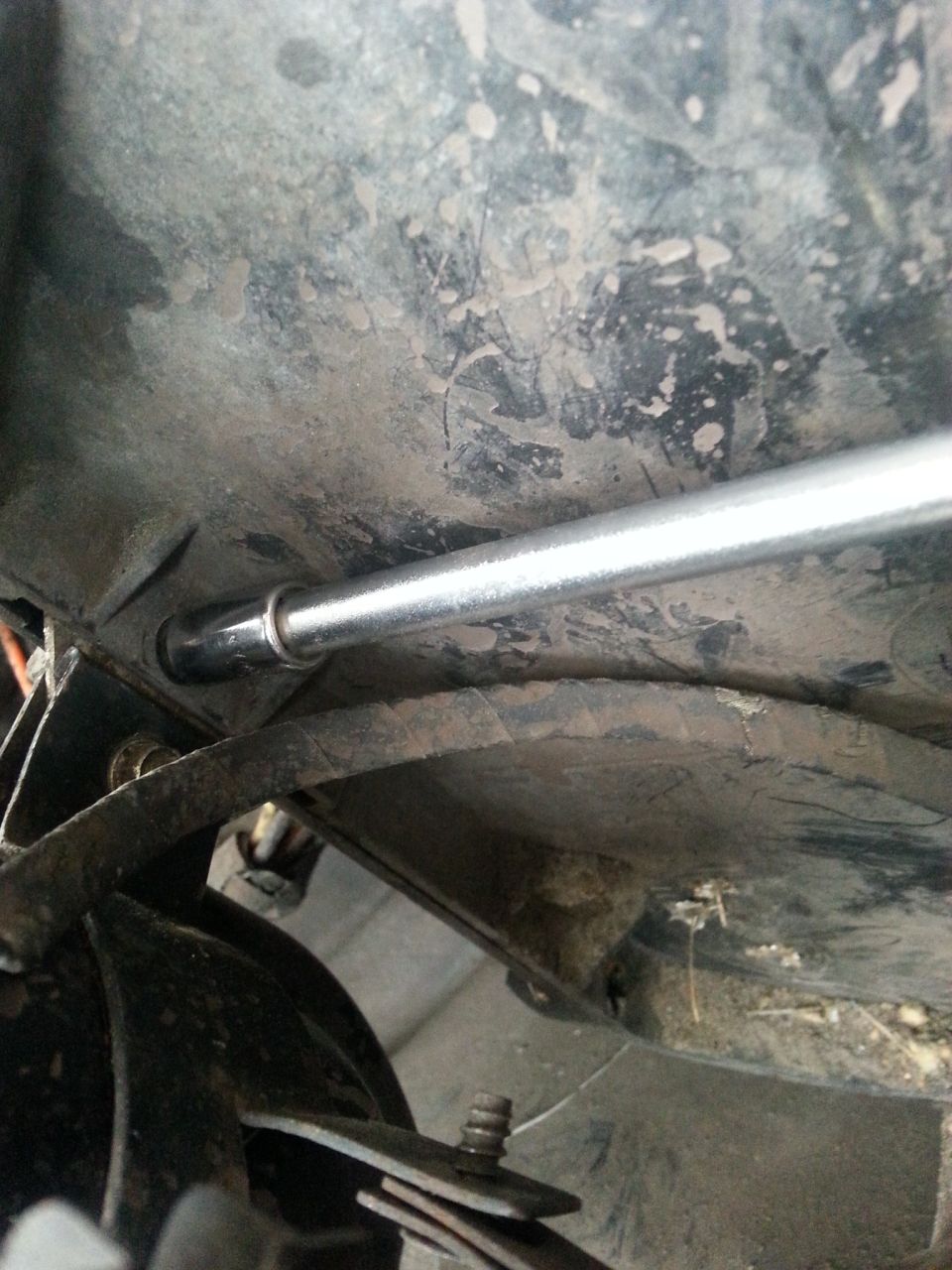 Screwdriver working on the underside of a vehicle, near a dusty metal panel