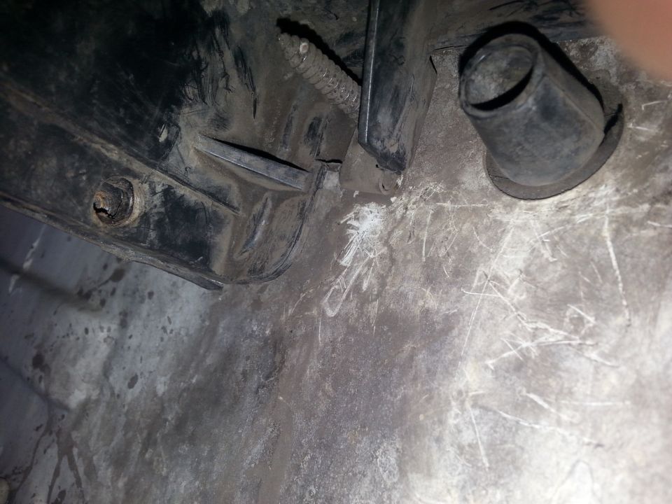 Black plastic automotive part with a metal bracket and a rubber grommet against a dirty concrete surface