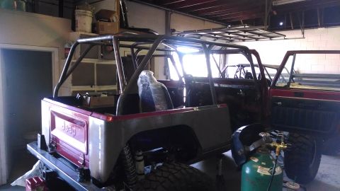 1985 Jeep CJ7 - A Jeep CJ is partially disassembled and fitted with a roll cage in a workshop setting.