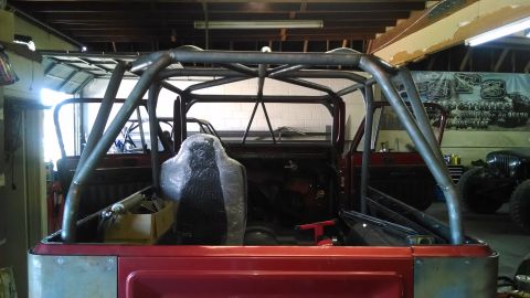1985 Jeep CJ7 - Interior view of a red Jeep CJ a custom roll cage and a seat covered in plastic.