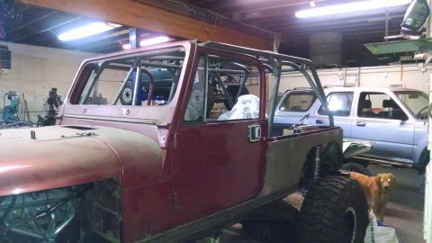 1985 Jeep CJ7 - A partially disassembled Jeep CJ-series is in a garage with another vehicle and a dog.
