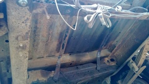 1983 Ford Bronco - The underside of a vehicle chassis shows significant rust and exposed wiring, with suspension components visible.