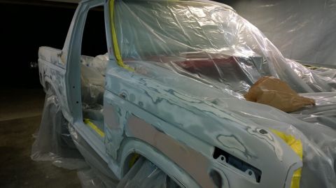 1983 Ford Bronco - Body of a 1983 Ford Bronco undergoing preparation for painting, with plastic sheeting and primer visible.