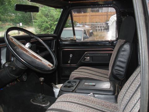 1979 Ford Bronco - The interior of a truck shows a worn steering wheel, patterned seats, and a floor shifter.