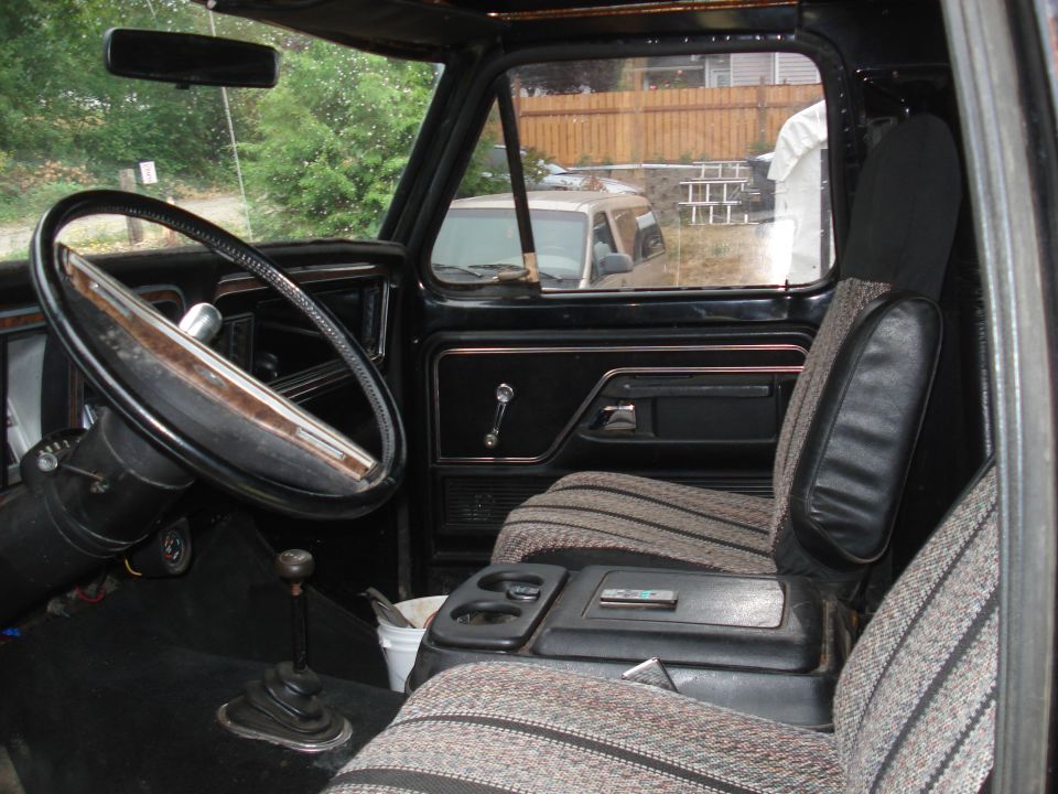 Interior view of a truck's dashboard, steering wheel, and seats. A white bucket is visible on the floor