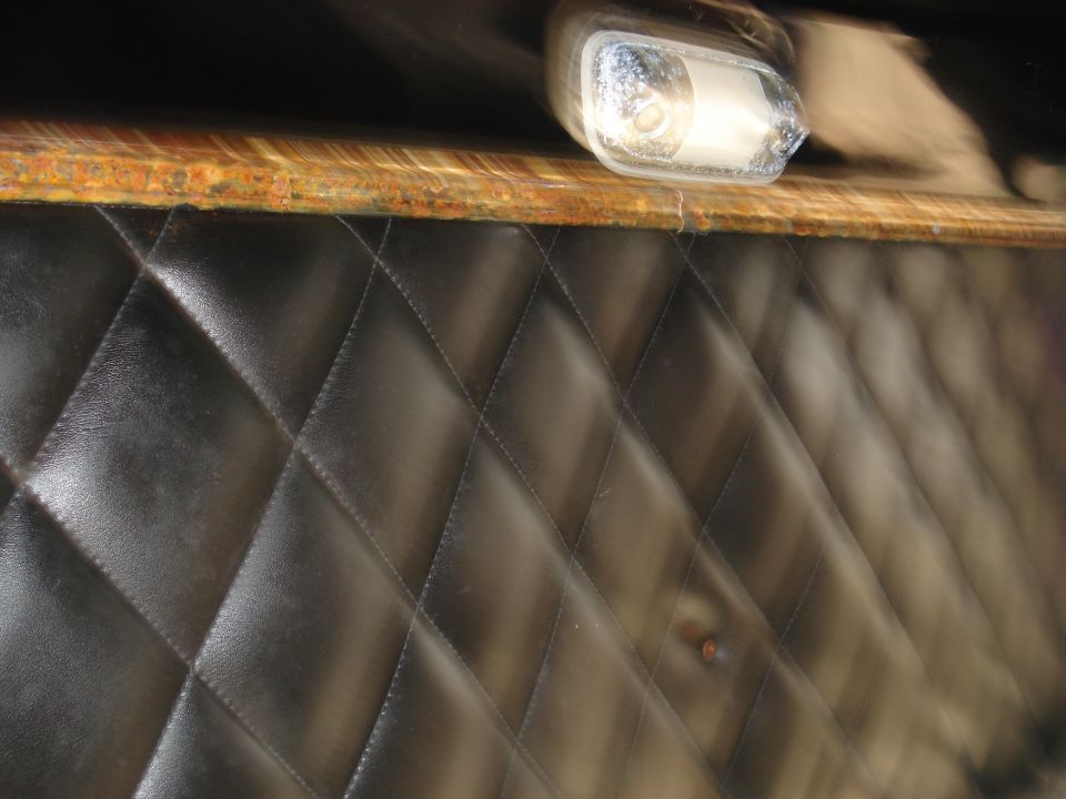 Black quilted upholstery panel with a chrome light fixture and wood trim above
