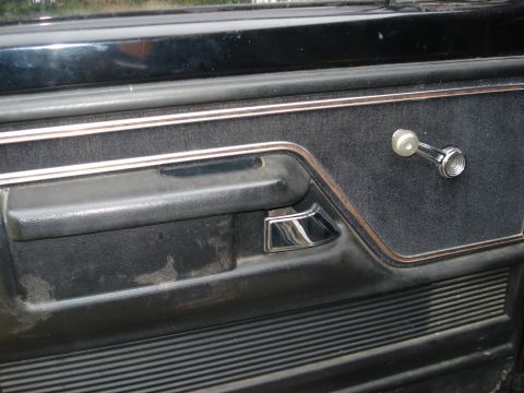 1979 Ford Bronco - Close-up of a vehicle's interior door panel, showing the window crank and door handle.