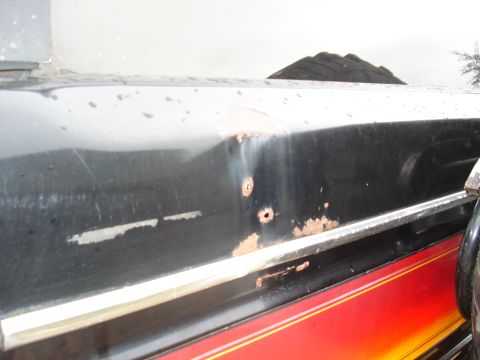 1979 Ford Bronco - Close-up of a black vehicle's side panel, revealing rust spots and damage, accented by a red and yellow stripe.