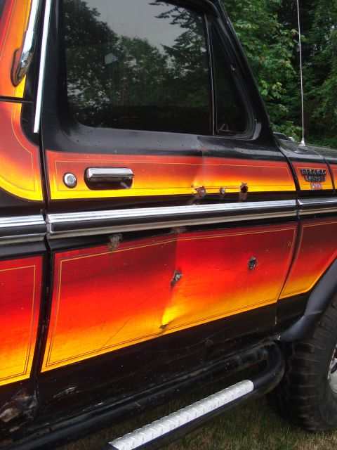 1979 Ford Bronco - Side view of a black 1978 Ford Bronco with a distinctive flame-like stripe and visible damage.