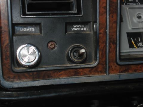 1979 Ford Bronco - Close-up of a vehicle's interior dashboard, wood grain trim and control buttons for lights and wipers.