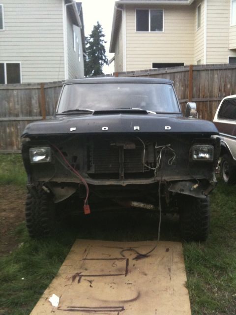 1979 Ford Bronco - Front view of a black 1979 Ford Bronco with its grille missing, parked in a grassy area with houses in the background.