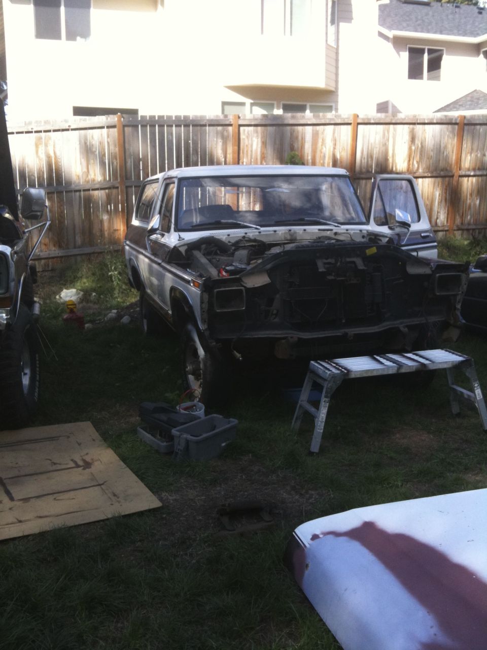 Two-tone brown and white Ford Bronco with hood open, parked in a yard