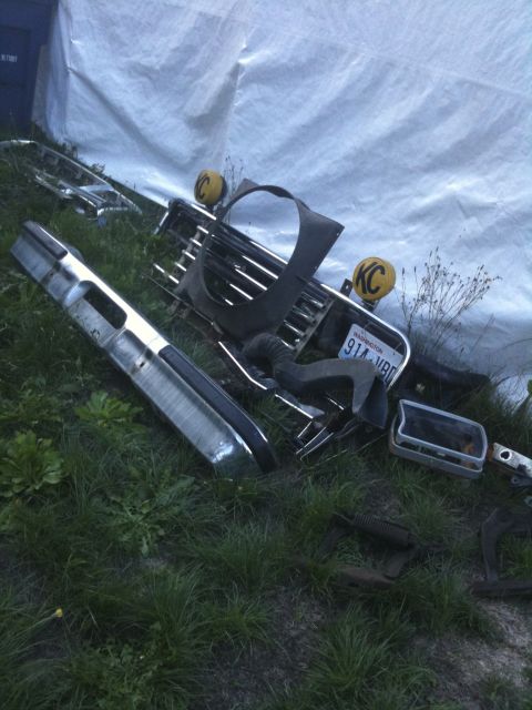 1979 Ford Bronco - Various vehicle parts, including a bumper and grille, are scattered on the grass.