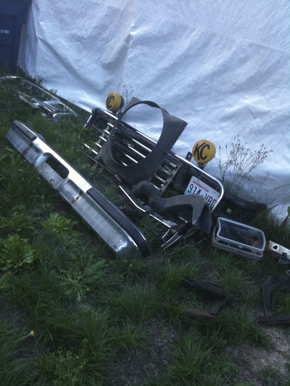 Bunch of car parts like a bumper and grille laid out on the grass