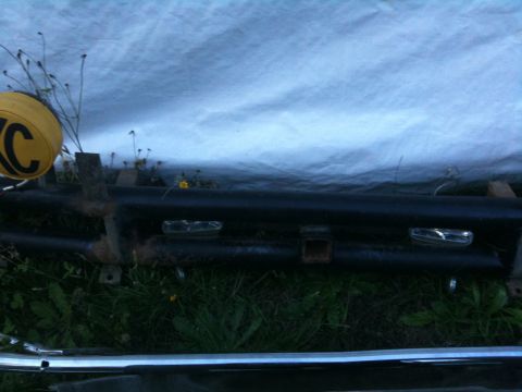 1979 Ford Bronco - A vehicle bumper with integrated lights and hitch receiver is visible, partially obscured by a tarp and overgrown grass.