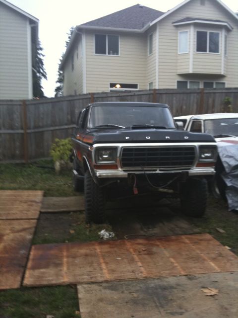 1979 Ford Bronco - A lifted black Ford Bronco sits in a yard with a wooden fence and houses in the background.