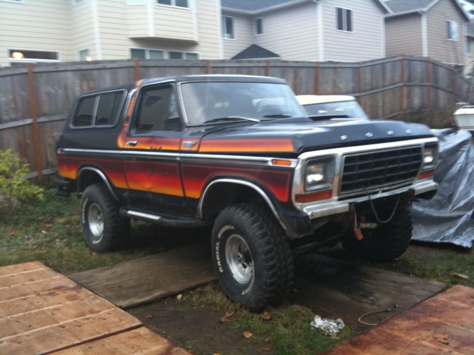 Black and orange 1978 Ford Bronco with lifted suspension and off-road tires parked on wooden planks