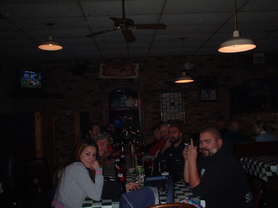 People gathered at tables in a dim bar with a Coca-Cola sign and TV