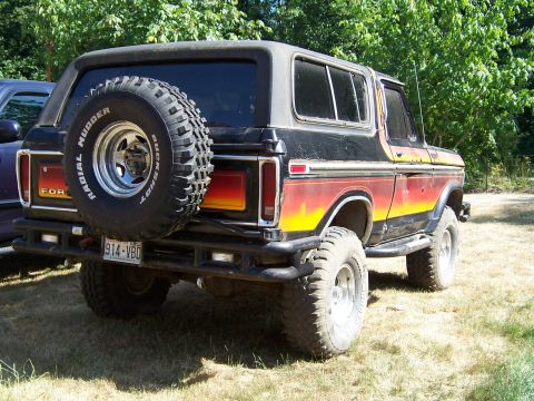 1979 Ford Bronco - This lifted Ford Bronco features a spare tire mounted on the rear door and a distinctive multi-colored stripe along its side.