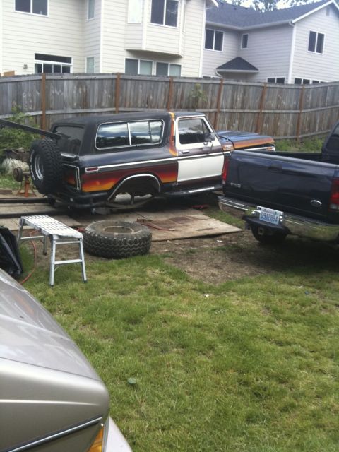 1979 Ford Bronco - A 1979 Ford Bronco is seen in a backyard, possibly undergoing repairs, alongside a dark blue pickup truck.