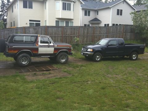 1979 Ford Bronco - Two Ford trucks, a classic Bronco and a modern F-150, sit in a grassy yard in front of a house.