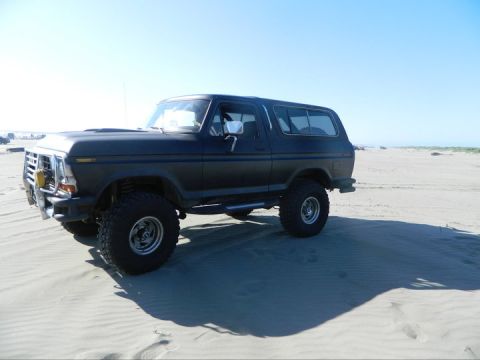 1979 Ford Bronco - A black Ford Bronco sits on a sandy beach under a clear blue sky, its lifted suspension and large tires ready for off-road adventure.
