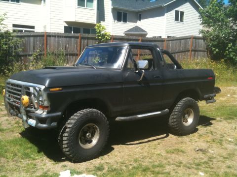 1979 Ford Bronco - Modified black Ford Bronco, likely from the late 1970s, sits in a yard.
